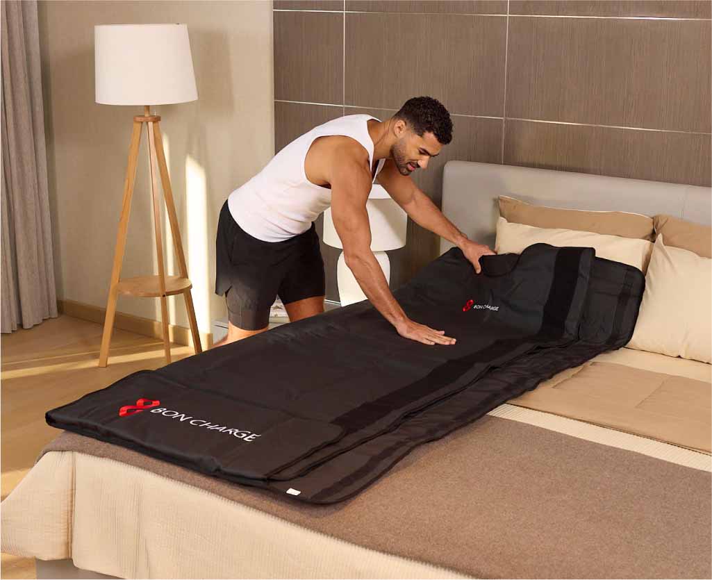 Man Rolling Out Sauna Blanket On Bed