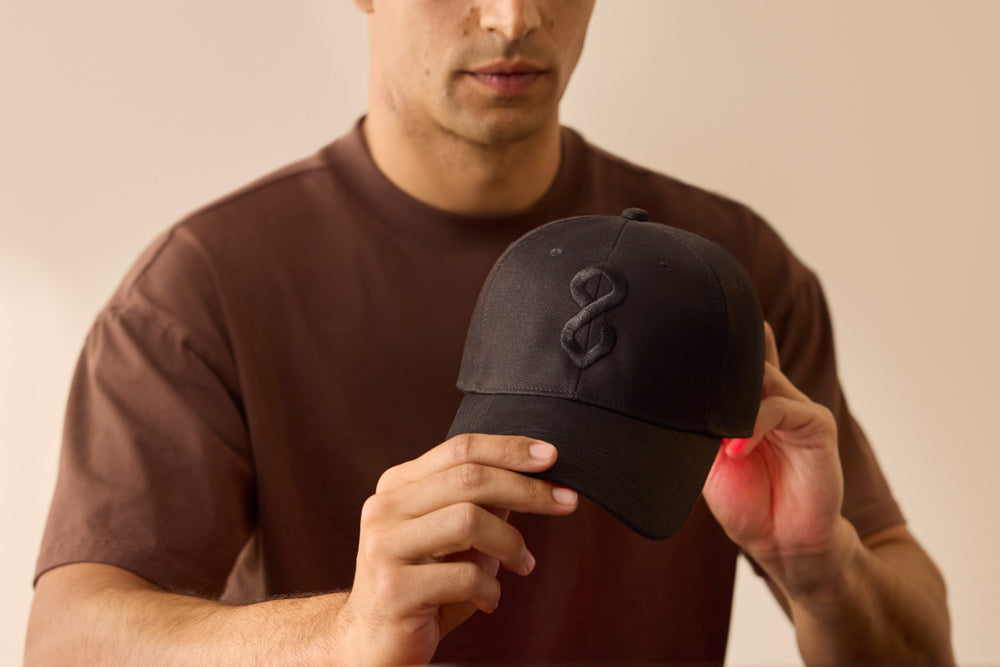 Man holding a black red light cap with logo, against a beige background
