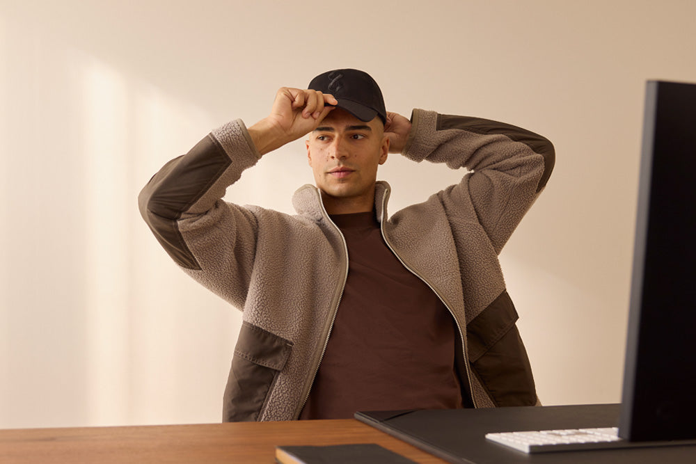 Man adjusting a cap in front of a computer screen with a neutral background